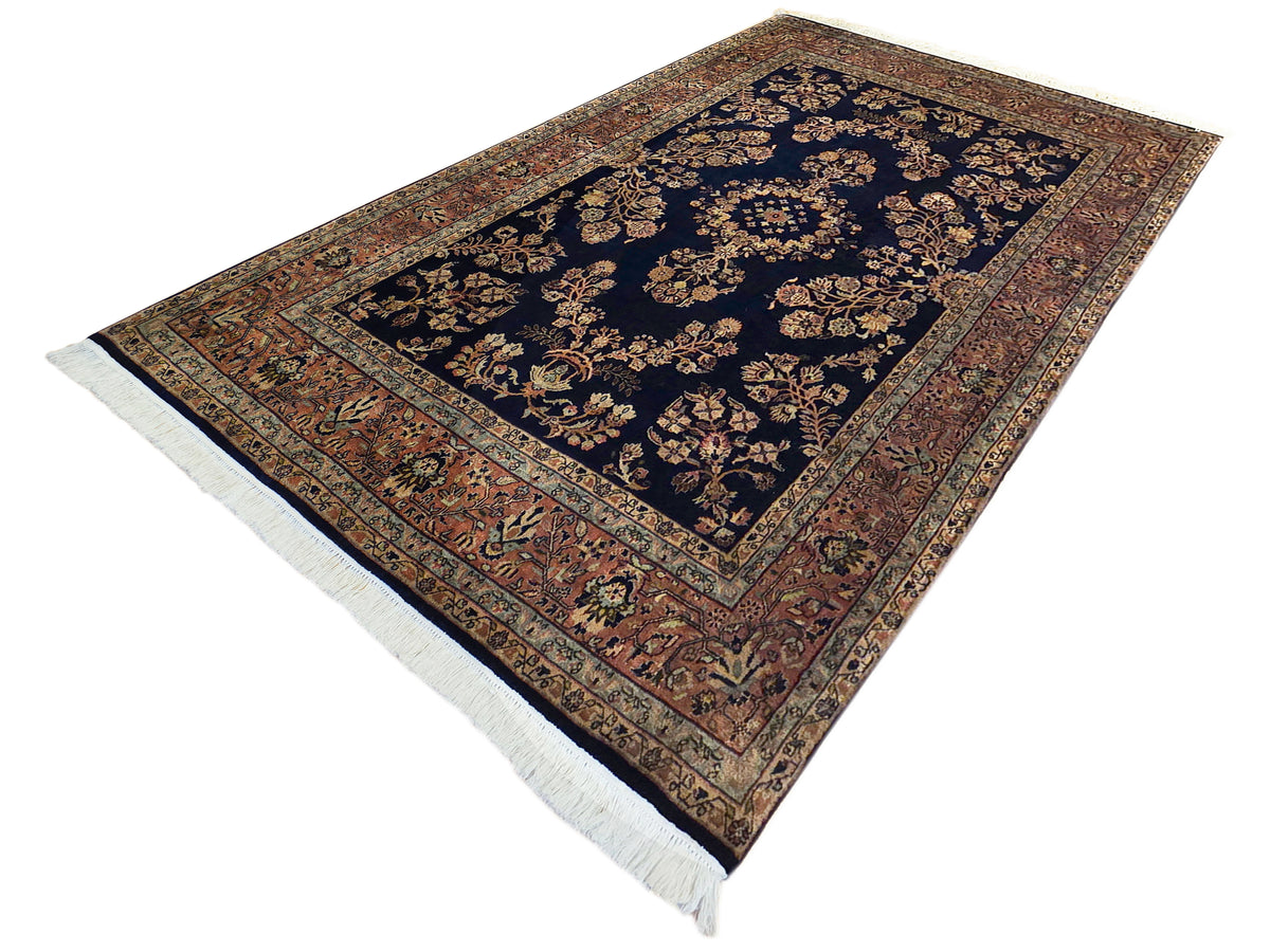 Sarouk rug with navy field, warm rust border, floral center medallion, fringed edges
