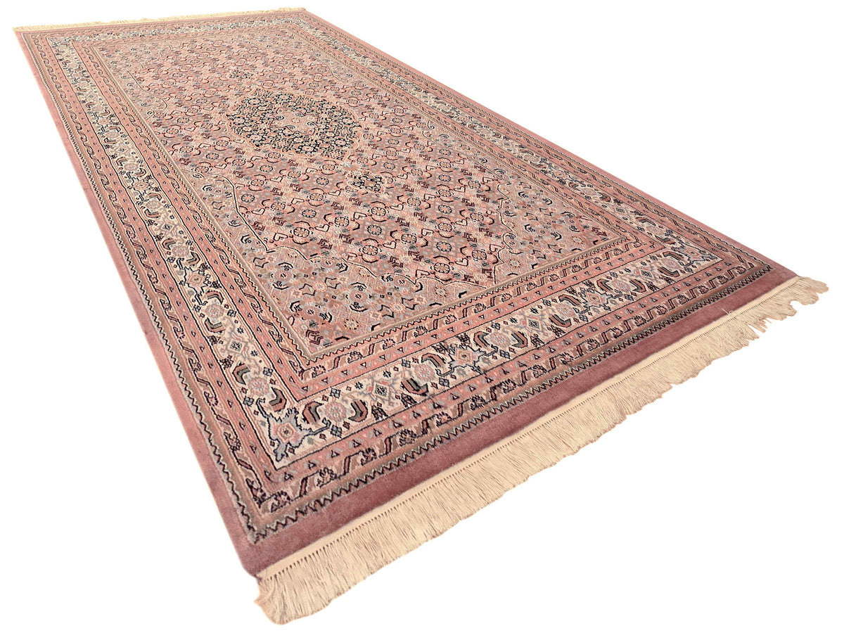 Bidjar rug wide angled view with dusty rose medallion, patterned border, and cream fringe