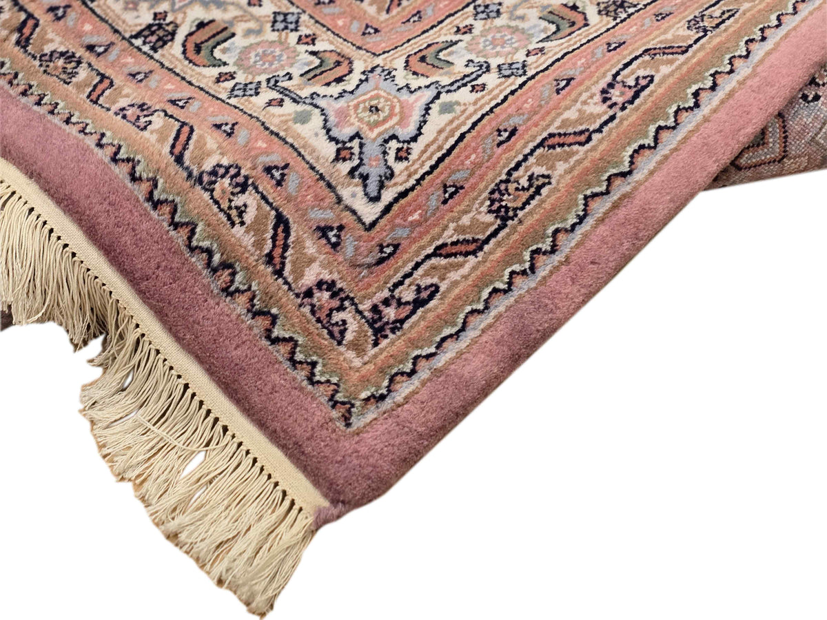 Bidjar rug corner close-up showing dusty rose pile, geometric motifs, and cream fringe