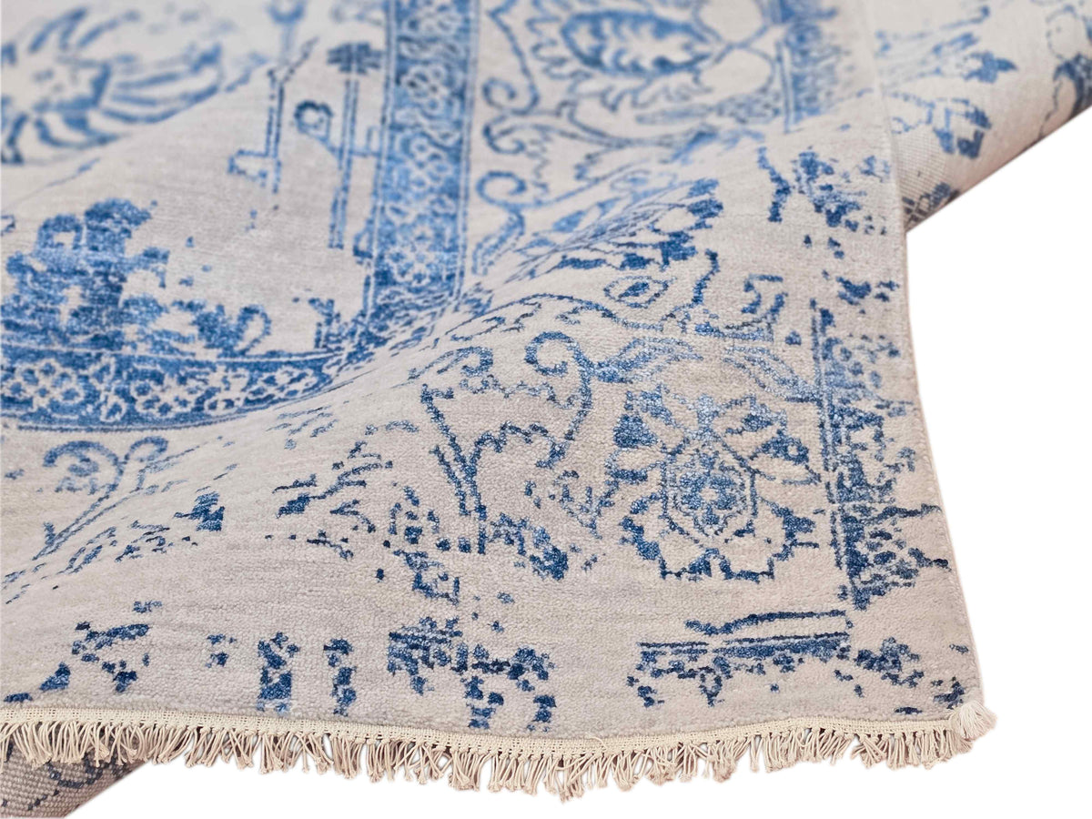 Corner detail of blue patterned rug on cream base with fringe trim
