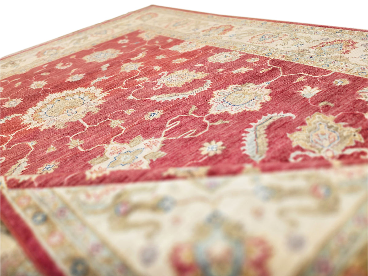 Close-up of red rug surface with cream floral scroll details and textured pile.