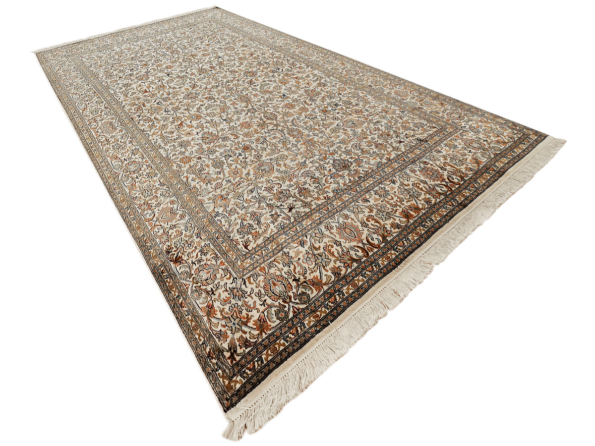 Beige patterned silk rug with central motif and dark geometric border, fringed corners