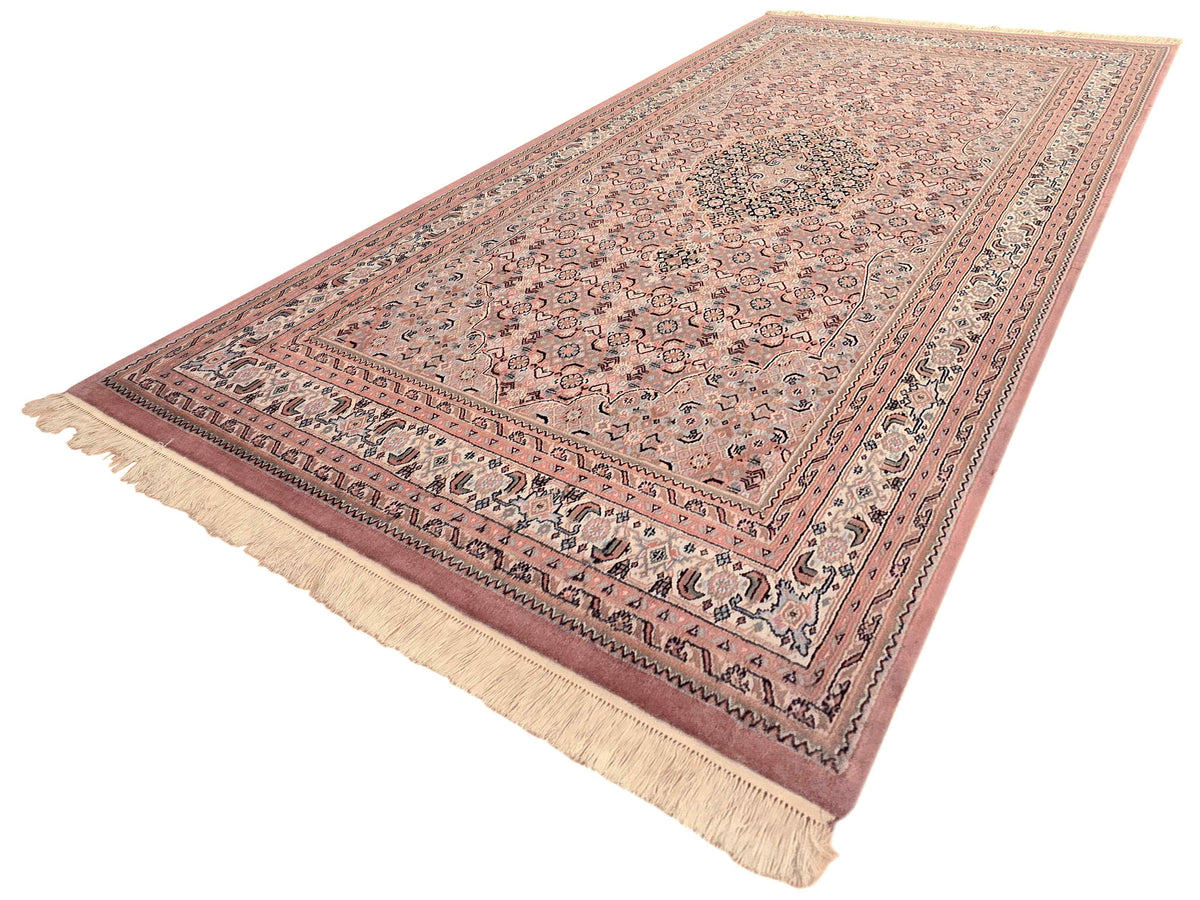 Bidjar rug angled view with dusty rose field, geometric motifs, and cream fringe border